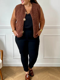 La veste moumoute sans manches Eda allie douceur et style. Conçue pour offrir un confort optimal, elle présente un col en V élégant et des broches dorées délicates sur le devant, qui ajoutent une touche sophistiquée.
