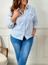Une chemise grande taille à rayures bleues et écrues avec des manches longues et un col chemise. Boutonnée sur le devant et aux poignets, elle possède des rayures verticales et une poche avec un noeud au niveau de la poitrine.