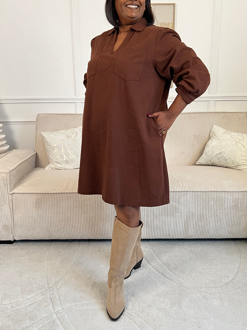 Cette robe courte en marron séduit par sa coupe ample et son col V à revers. Dotée de manches longues, de poches pratiques et de détails dorés aux poignets, elle allie confort et style au quotidien.