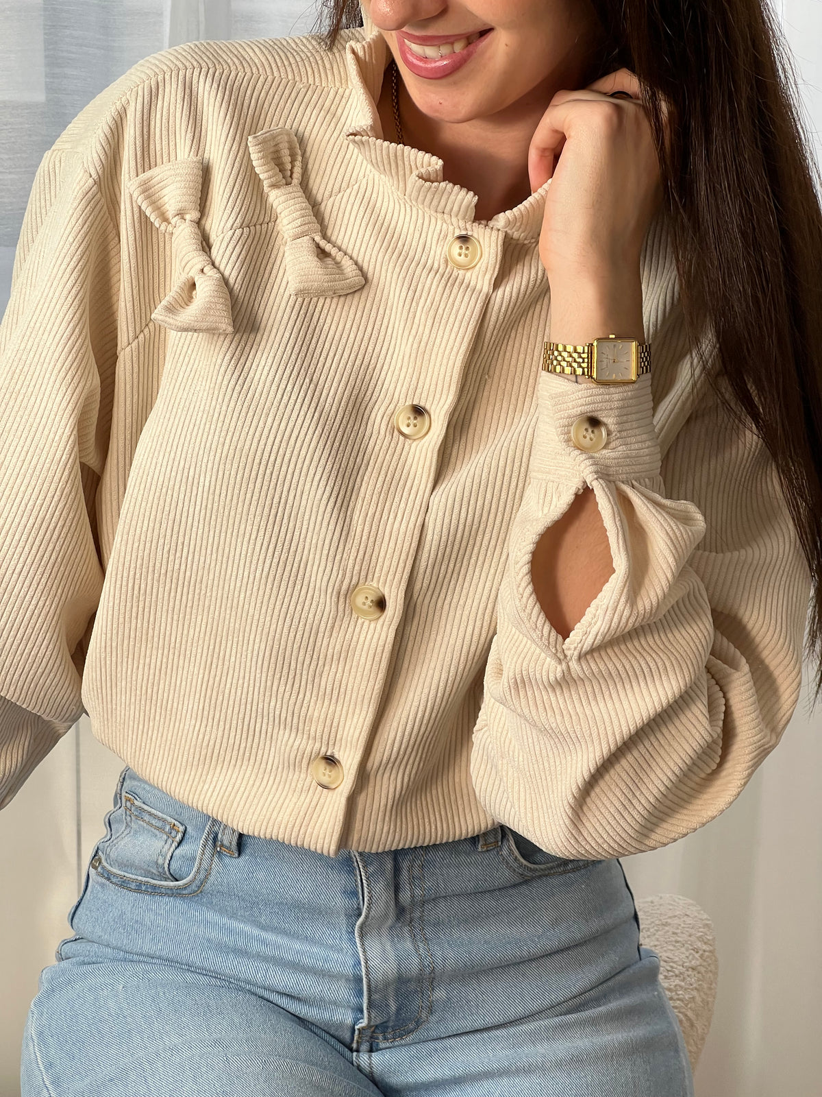 Chemise beige en velours côtelé pour femme, dotée de manches longues et d'un col rond orné de volants. Nœuds latéraux et boutons discrets sur toute la longueur et aux poignets pour un style raffiné et élégant.