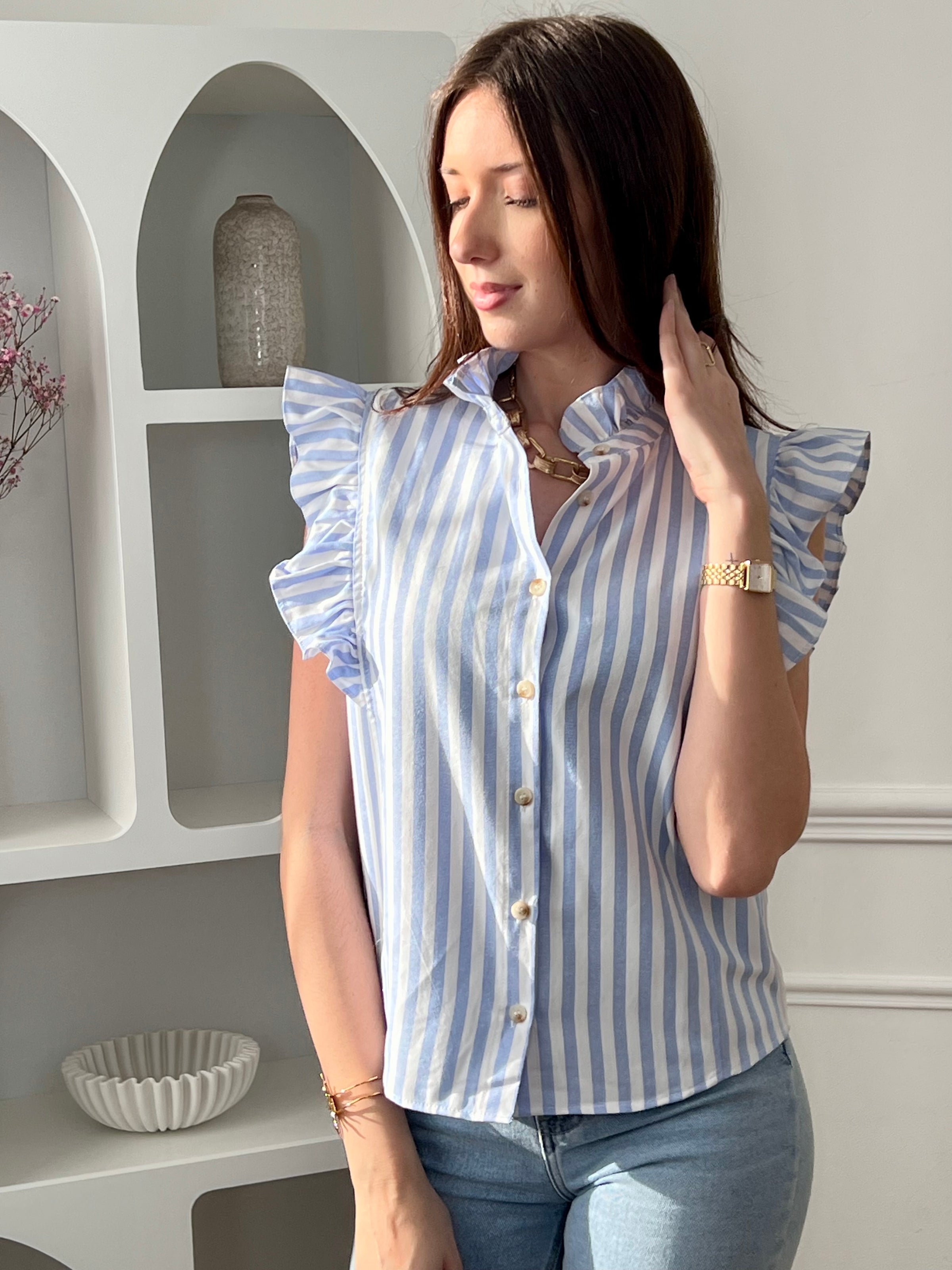 Adoptez cette chemise bleue et écrue femme sans manches, légère et élégante. Elle se ferme par des boutons sur toute la longueur et se distingue par ses volants au col et aux épaules, apportant une touche féminine. Ses rayures verticales en bleu et écru allongent la silhouette et subliment vos tenues.