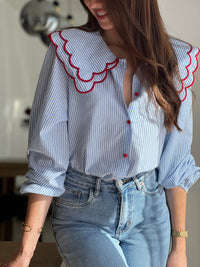 Chemise femme bleue à rayures avec col claudine, parfaite pour un look élégant et féminin. Ses manches longues et ses boutons rouges sur toute la longueur apportent une touche originale et raffinée. L’association des couleurs bleu, blanc et rouge crée un style chic et intemporel. Idéale pour une tenue moderne, aussi bien au bureau qu’au quotidien.
