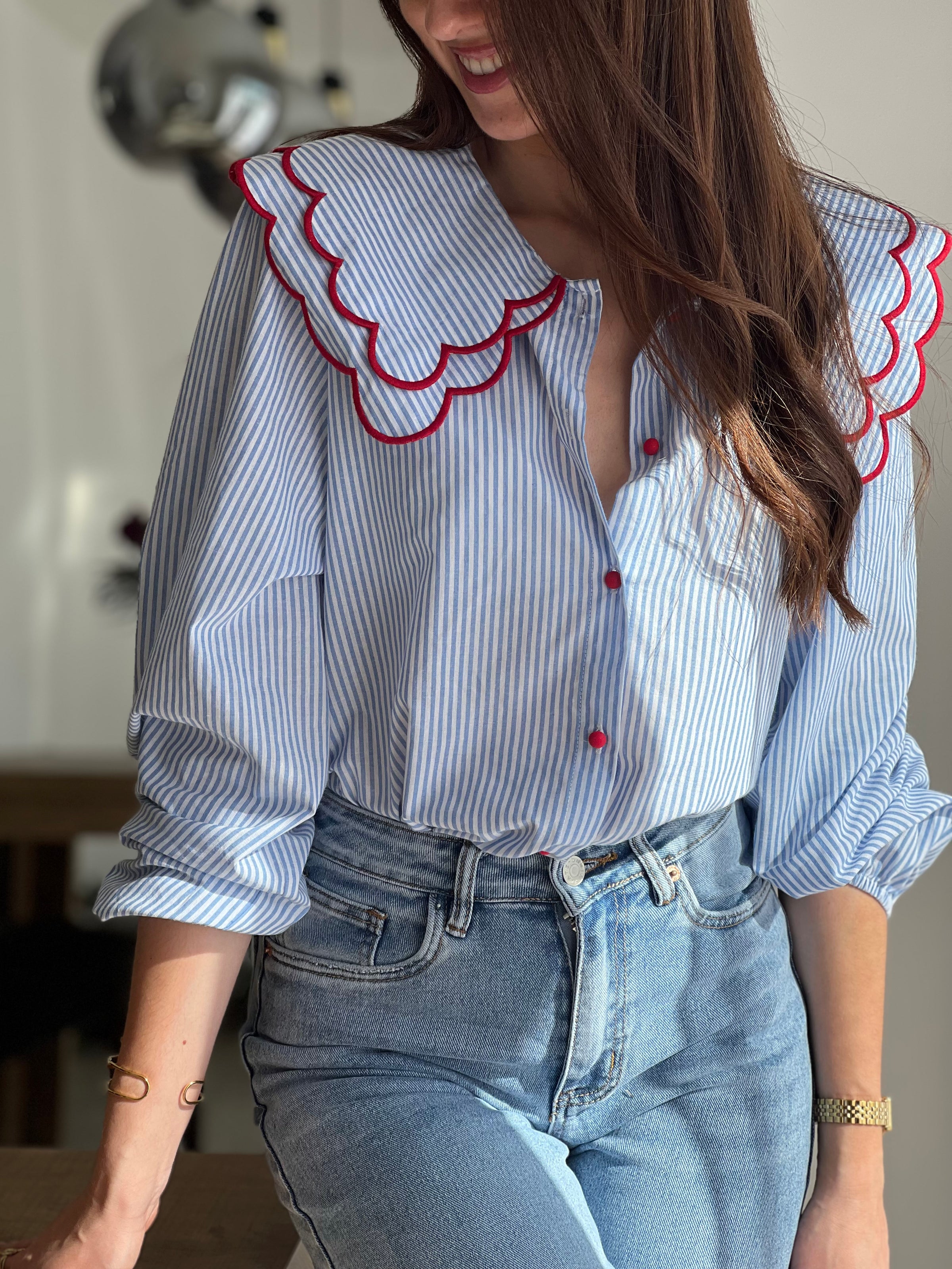 Chemise femme bleue à rayures avec col claudine, parfaite pour un look élégant et féminin. Ses manches longues et ses boutons rouges sur toute la longueur apportent une touche originale et raffinée. L’association des couleurs bleu, blanc et rouge crée un style chic et intemporel. Idéale pour une tenue moderne, aussi bien au bureau qu’au quotidien.