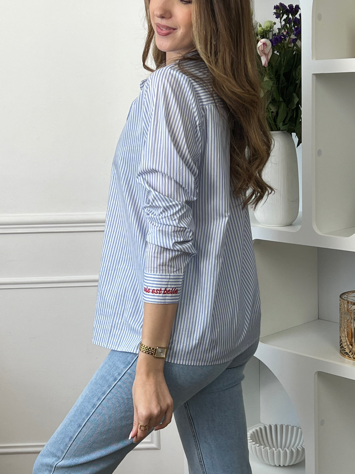 Chemise en coton femme, parfaite pour un look à la fois élégant et original. Dotée de manches longues, d’un col chemise et de boutons rouges sur toute la longueur ainsi qu’aux poignets, elle se distingue par ses rayures verticales bleues et écrues. Ses détails brodés, avec des cœurs au col et l’inscription "La vie est belle" aux poignets, apportent une touche unique et tendance