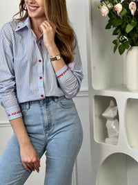 Chemise en coton femme, parfaite pour un look à la fois élégant et original. Dotée de manches longues, d’un col chemise et de boutons rouges sur toute la longueur ainsi qu’aux poignets, elle se distingue par ses rayures verticales bleues et écrues. Ses détails brodés, avec des cœurs au col et l’inscription "La vie est belle" aux poignets, apportent une touche unique et tendance