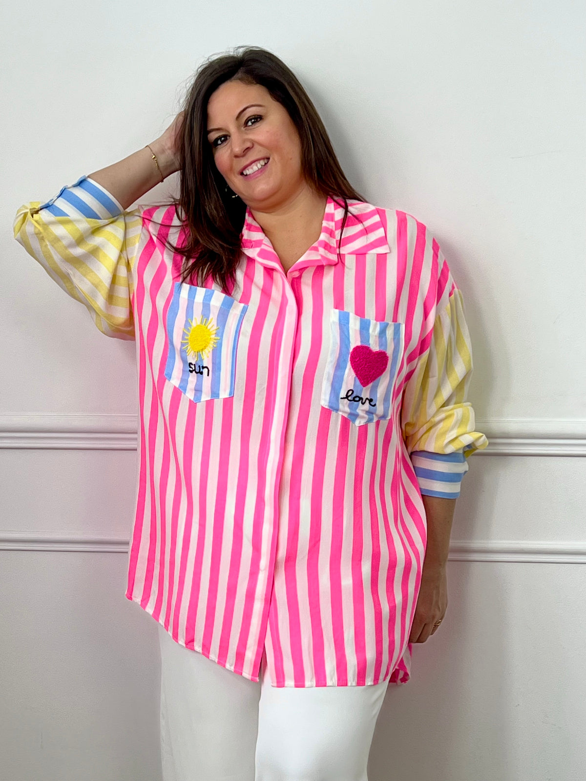 Chemise grande taille colorée au style oversize, idéale pour un look tendance et décontracté. Avec sa coupe longue, légèrement plus étendue au dos, ses manches longues et son col chemise classique, elle allie confort et modernité. Dotée de boutons sur toute la longueur, de poignets boutonnés et de deux poches poitrine, elle se distingue par ses rayures roses, jaunes, bleues et écrues ainsi que ses broderies originales "sun", "love", cœur et soleil.