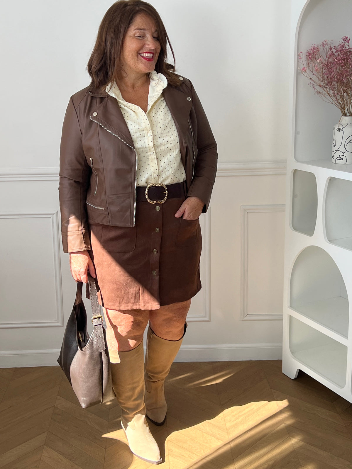 Chemise beige Sofia portée sous une veste marron, avec une jupe assortie et des bottes beiges.