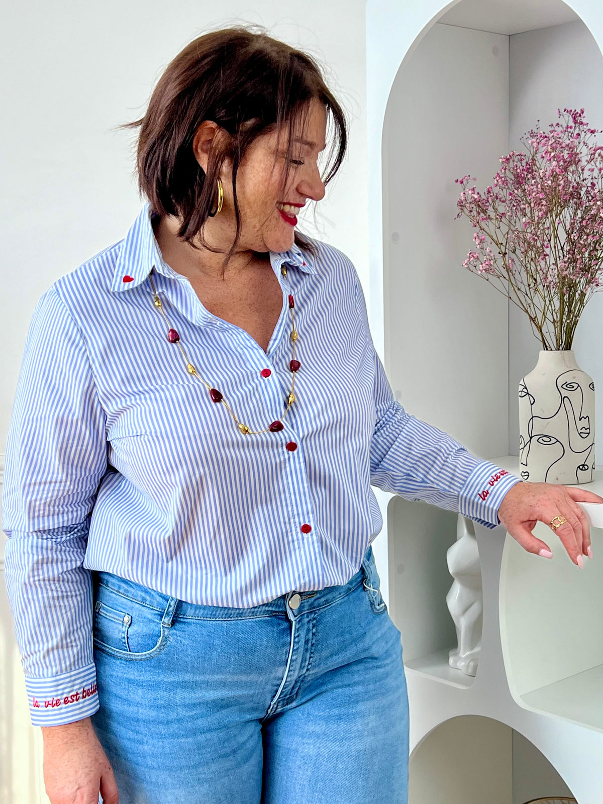 Chemise en coton grande taille femme, parfaite pour un look à la fois élégant et original. Dotée de manches longues, d’un col chemise et de boutons rouges sur toute la longueur ainsi qu’aux poignets, elle se distingue par ses rayures verticales bleues et écrues. Ses détails brodés, avec des cœurs au col et l’inscription "La vie est belle" aux poignets, apportent une touche unique et tendance