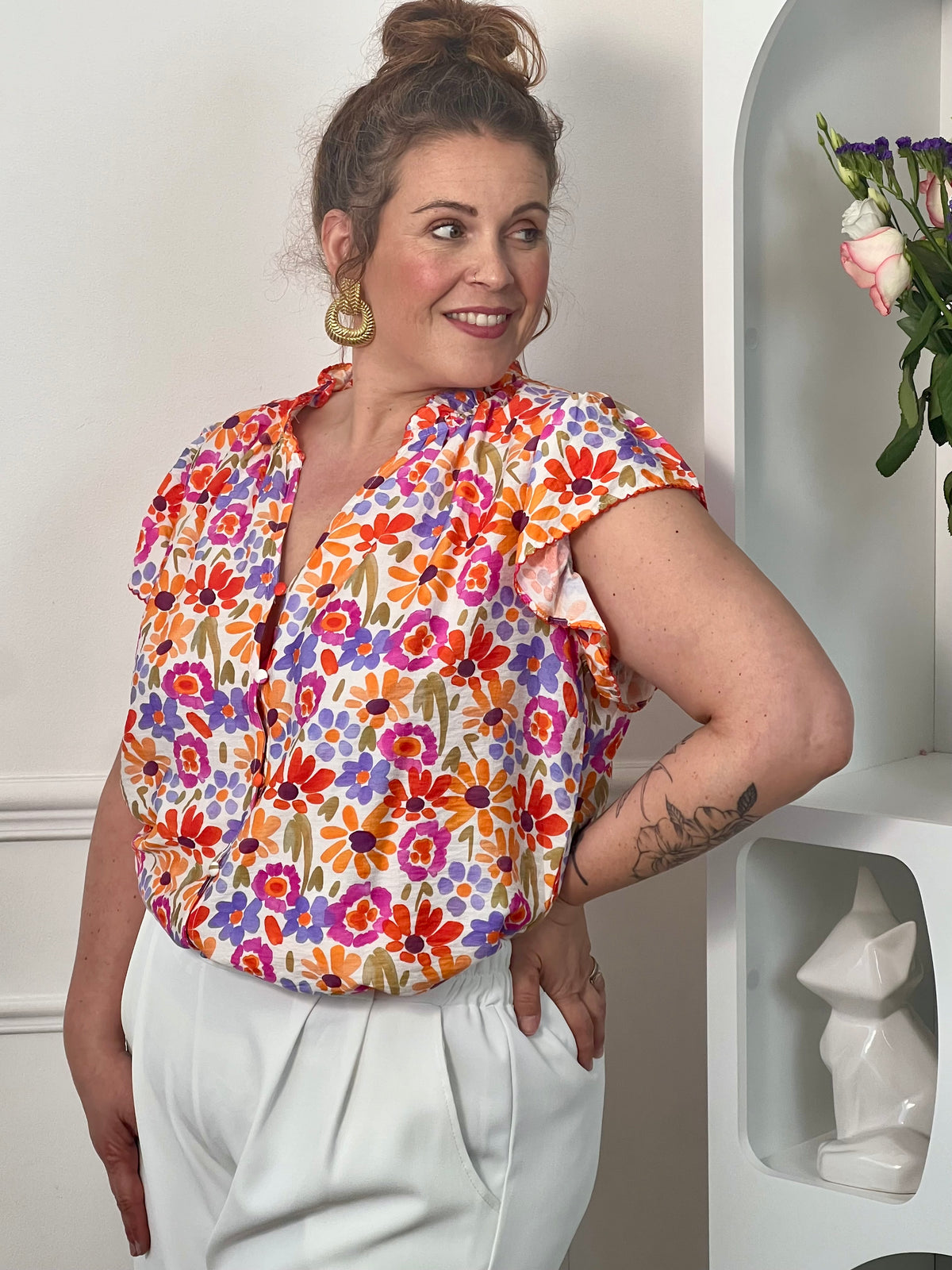 Chemise à motifs grande taille femme, parfaite pour un look féminin et tendance. Sans manches, avec un col V et des boutons sur toute la longueur, elle allie élégance et confort. Ses volants au niveau des épaules et du col apportent une touche raffinée, tandis que ses motifs fleurs aux tons orange, vert, violet, rose et écru illuminent la silhouette. Une chemise fluide idéale pour une tenue chic et estivale.