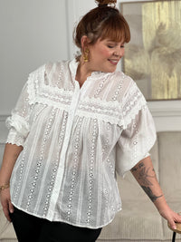 Chemise Angele en coton 100% pour les femmes grandes tailles. Manches bouffantes, col volant et broderie ajourée confèrent à cette pièce écrue une élégance intemporelle. Légèrement transparente, elle se porte avec aisance au quotidien comme en occasion.