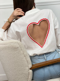 Chemise en coton aux détails romantiques et féminins. Manches longues avec boutons aux poignets, col chemise classique et fermeture boutonnée sur toute la longueur. La touche signature : une découpe en cœur rouge au dos qui ajoute une dimension poétique à cette pièce incontournable. Parfaite pour créer des looks à la fois élégants et originaux.
