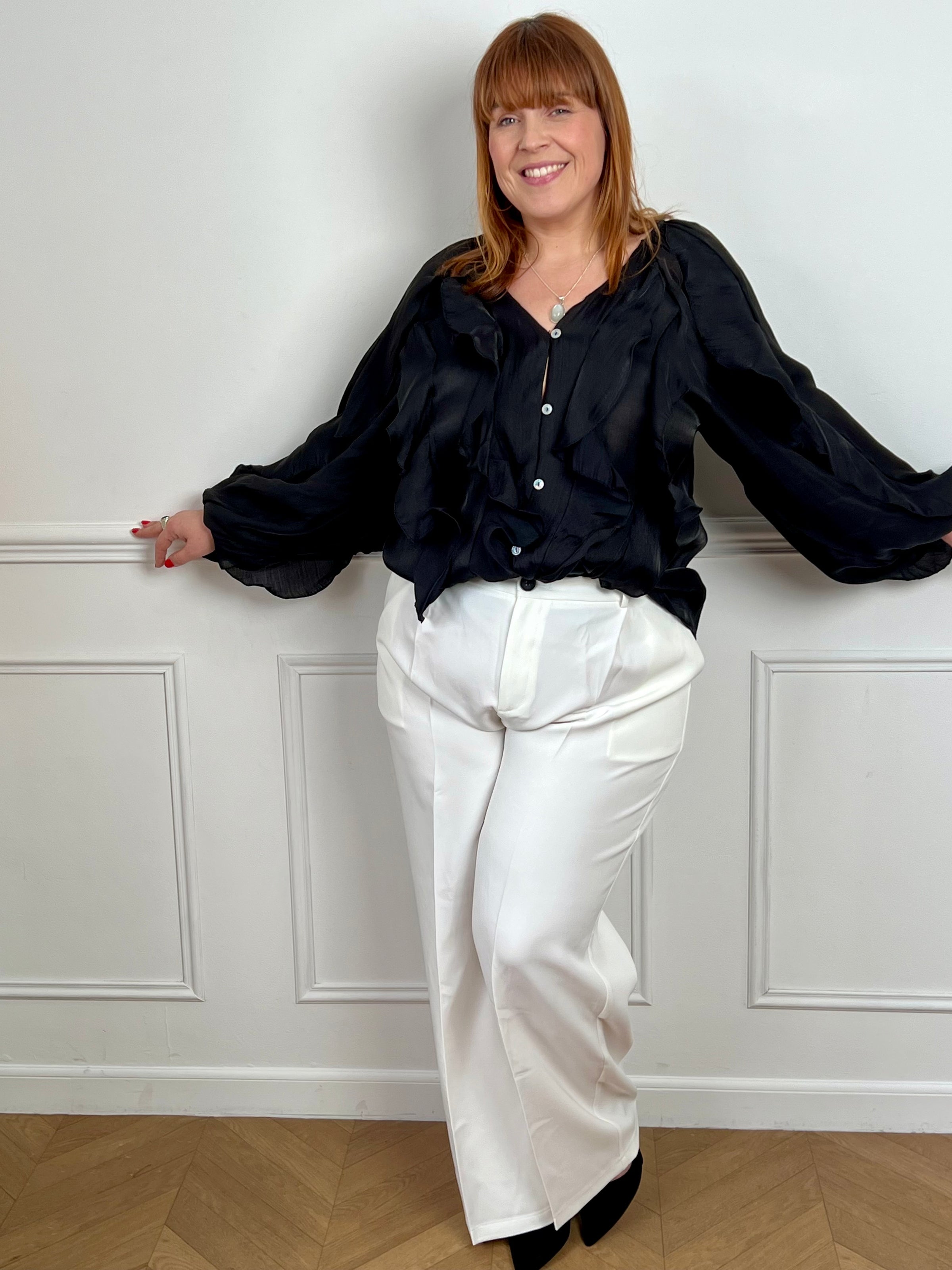 Légère et pleine de charme, cette chemise noire pour femme apporte une touche lumineuse et féminine à votre tenue. Son col V délicatement souligné par un élastique met en valeur le décolleté, tandis que les poignets élastiqués assurent un joli tombé aux manches longues. Les volants au col, aux épaules et aux manches ajoutent du mouvement et une note romantique à l’ensemble. Sa matière légèrement transparente renforce son côté aérien et élégant.