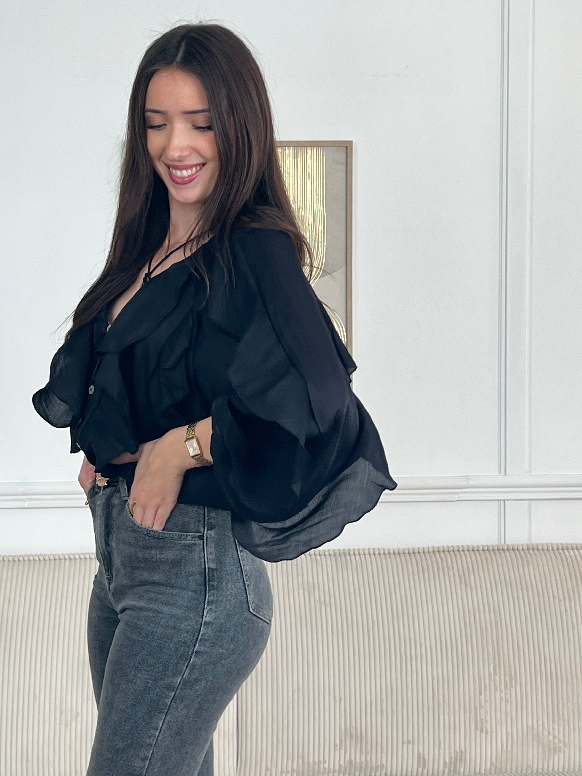 Légère et pleine de charme, cette chemise noire pour femme apporte une touche lumineuse et féminine à votre tenue. Son col V délicatement souligné par un élastique met en valeur le décolleté, tandis que les poignets élastiqués assurent un joli tombé aux manches longues. Les volants au col, aux épaules et aux manches ajoutent du mouvement et une note romantique à l’ensemble. Sa matière légèrement transparente renforce son côté aérien et élégant.