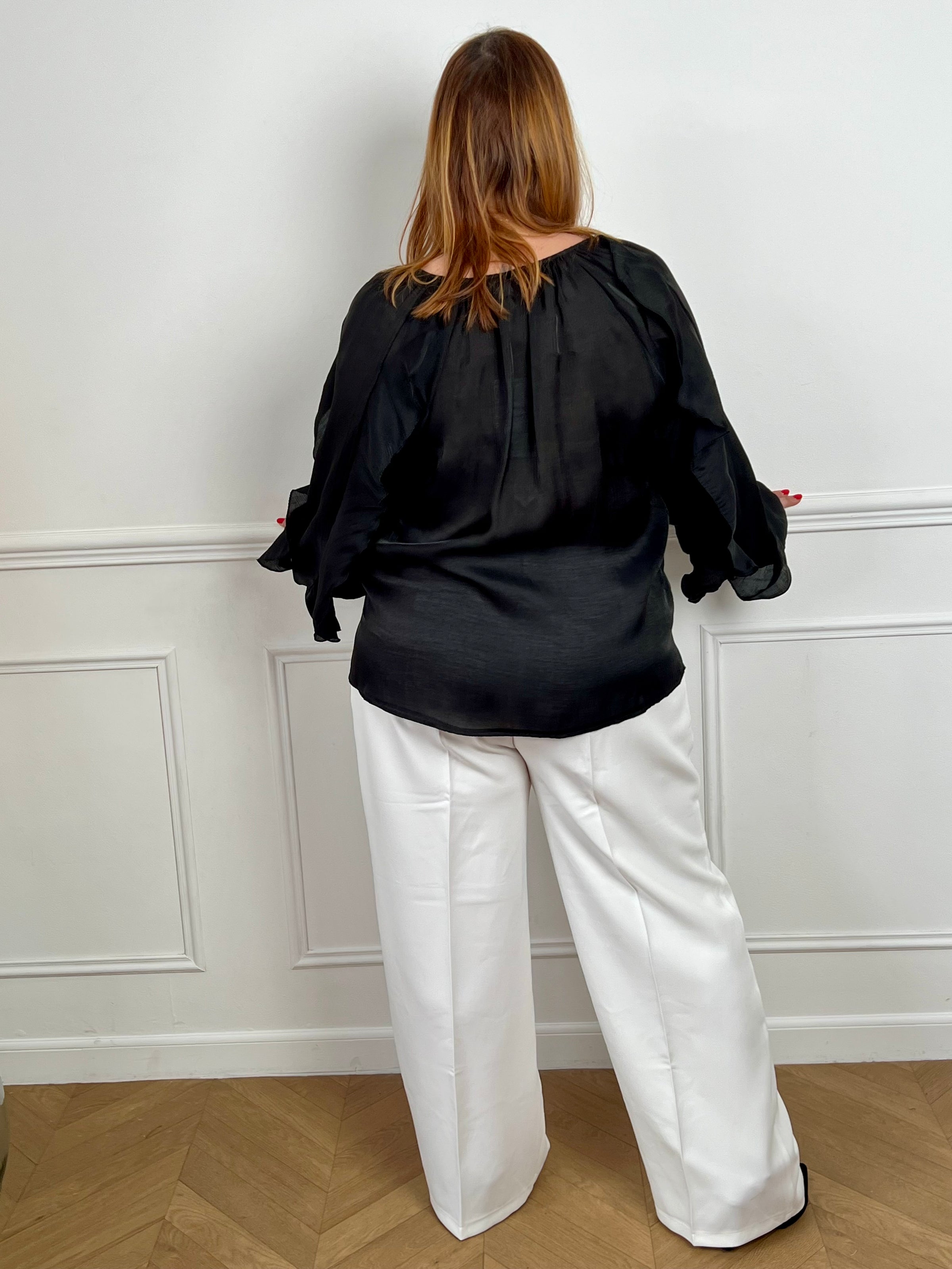 Légère et pleine de charme, cette chemise noire pour femme apporte une touche lumineuse et féminine à votre tenue. Son col V délicatement souligné par un élastique met en valeur le décolleté, tandis que les poignets élastiqués assurent un joli tombé aux manches longues. Les volants au col, aux épaules et aux manches ajoutent du mouvement et une note romantique à l’ensemble. Sa matière légèrement transparente renforce son côté aérien et élégant.