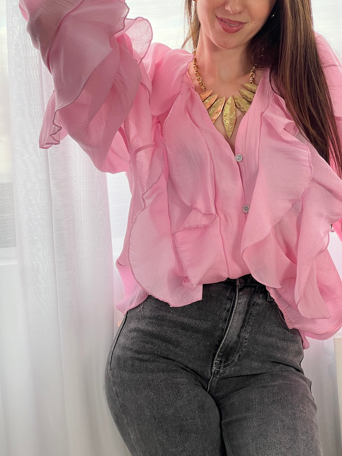 Légère et pleine de charme, cette chemise rose pour femme apporte une touche lumineuse et féminine à votre tenue. Son col V délicatement souligné par un élastique met en valeur le décolleté, tandis que les poignets élastiqués assurent un joli tombé aux manches longues. Les volants au col, aux épaules et aux manches ajoutent du mouvement et une note romantique à l’ensemble. Sa matière légèrement transparente renforce son côté aérien et élégant.