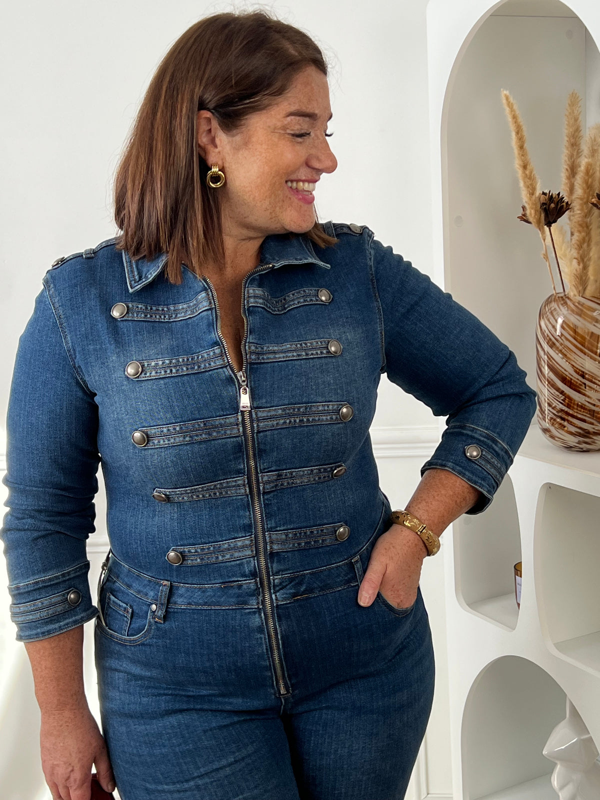 Gros plan sur le col, le zip et les pattes décoratives à boutons métalliques de la combinaison en jean bleu – Nella | Loïcia