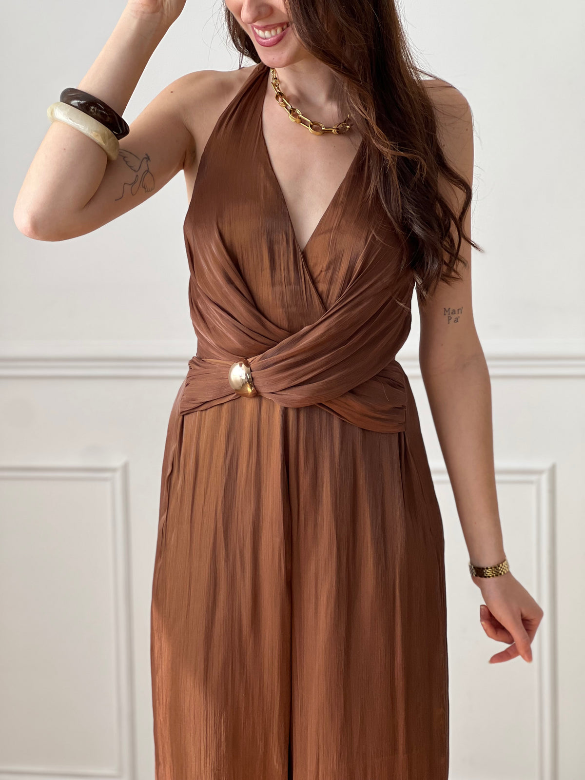 Cette combinaison satinée marron séduit par son élégance et sa fluidité. Son col en V met en valeur le décolleté, tandis que le lien nouable à la nuque apporte une touche féminine et raffinée. Idéale pour un look chic et sophistiqué.