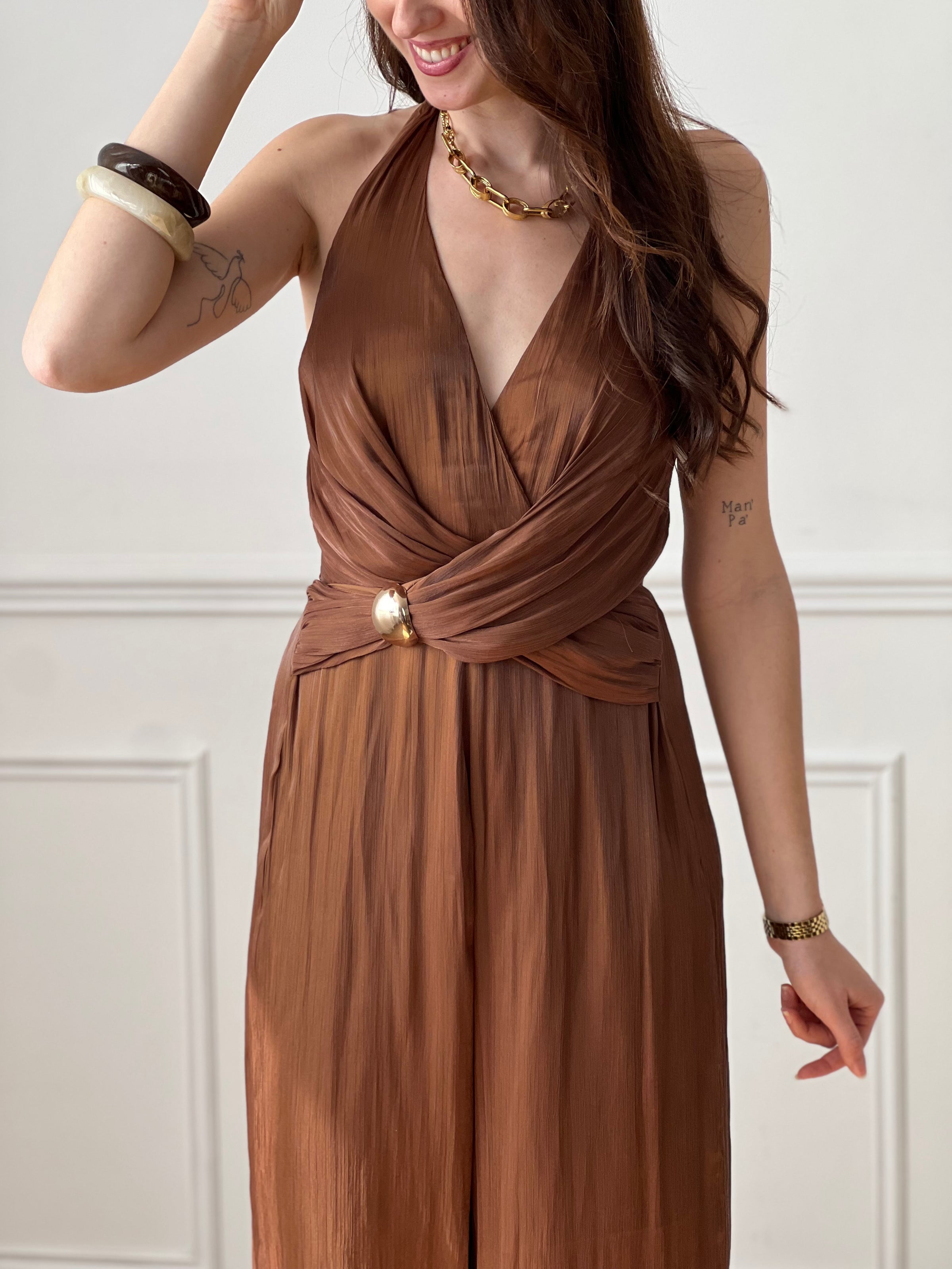 Cette combinaison satinée marron séduit par son élégance et sa fluidité. Son col en V met en valeur le décolleté, tandis que le lien nouable à la nuque apporte une touche féminine et raffinée. Idéale pour un look chic et sophistiqué.
