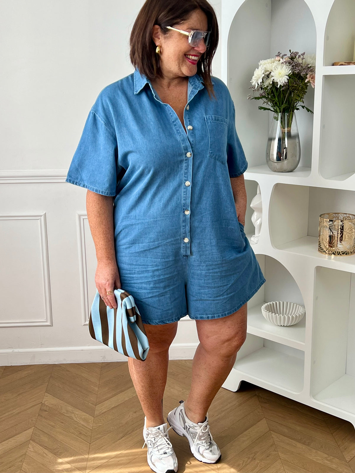 Combishort en jean grande taille, idéal pour un look casual et confortable. Doté d’un col chemise, de manches courtes et d’une coupe ample, il offre une silhouette moderne et décontractée. Avec sa poche poitrine, ses deux poches latérales et ses boutons jusqu’à mi-longueur, il allie style et praticité. Confectionné en 100% coton, ce combishort bleu est parfait pour une tenue tendance au quotidien.