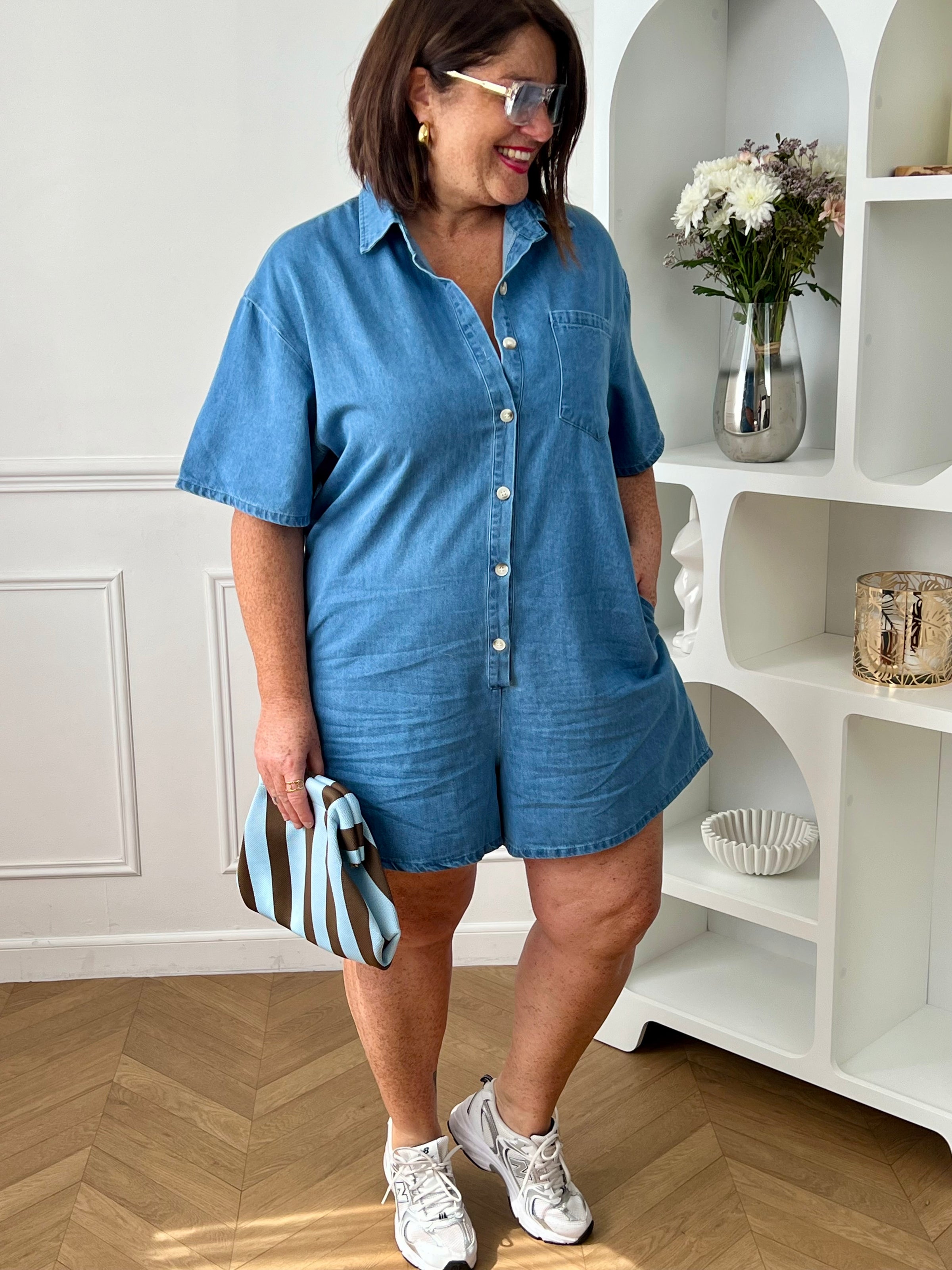 Combishort en jean grande taille, idéal pour un look casual et confortable. Doté d’un col chemise, de manches courtes et d’une coupe ample, il offre une silhouette moderne et décontractée. Avec sa poche poitrine, ses deux poches latérales et ses boutons jusqu’à mi-longueur, il allie style et praticité. Confectionné en 100% coton, ce combishort bleu est parfait pour une tenue tendance au quotidien.