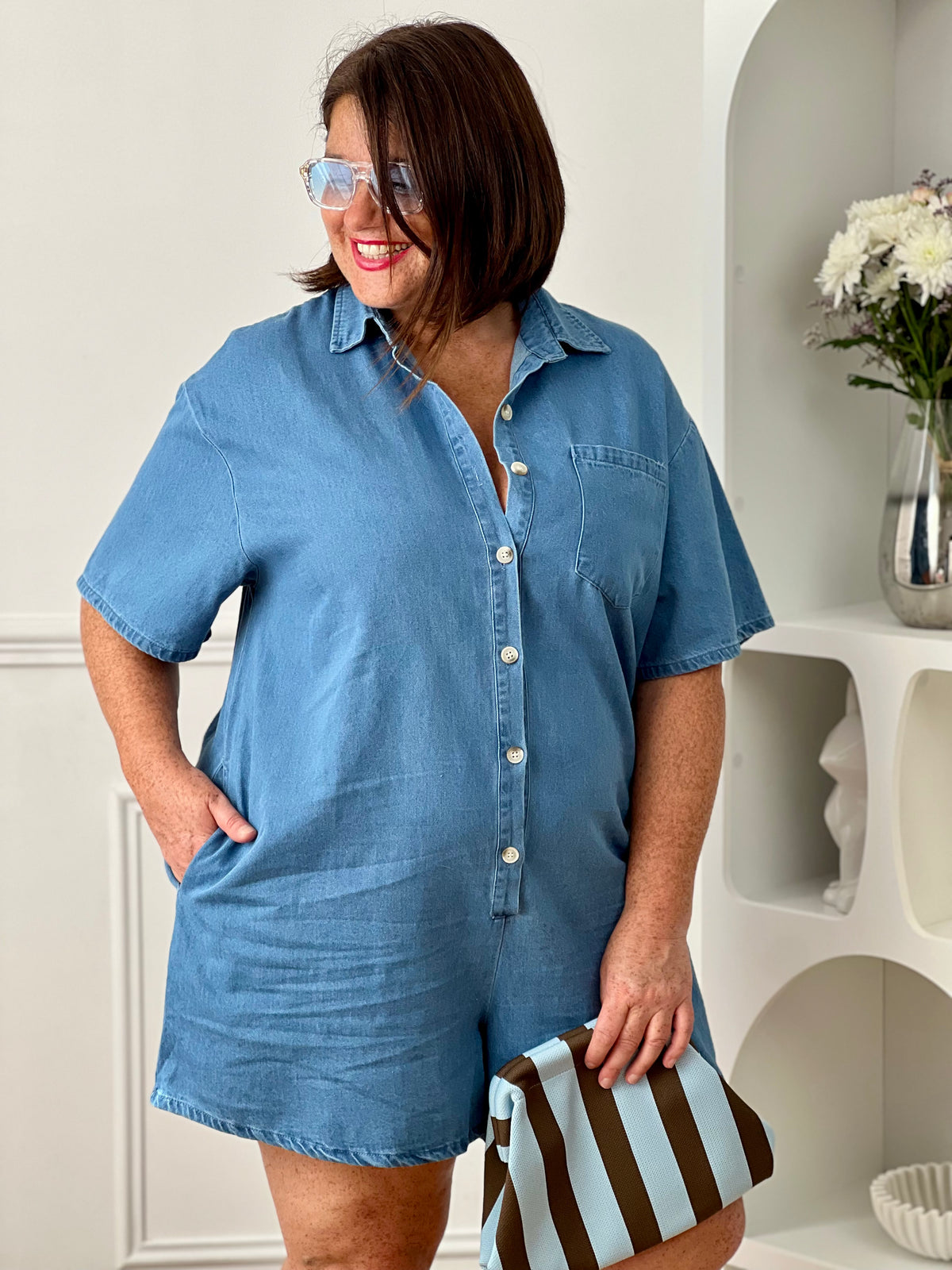 Combishort en jean grande taille, idéal pour un look casual et confortable. Doté d’un col chemise, de manches courtes et d’une coupe ample, il offre une silhouette moderne et décontractée. Avec sa poche poitrine, ses deux poches latérales et ses boutons jusqu’à mi-longueur, il allie style et praticité. Confectionné en 100% coton, ce combishort bleu est parfait pour une tenue tendance au quotidien.