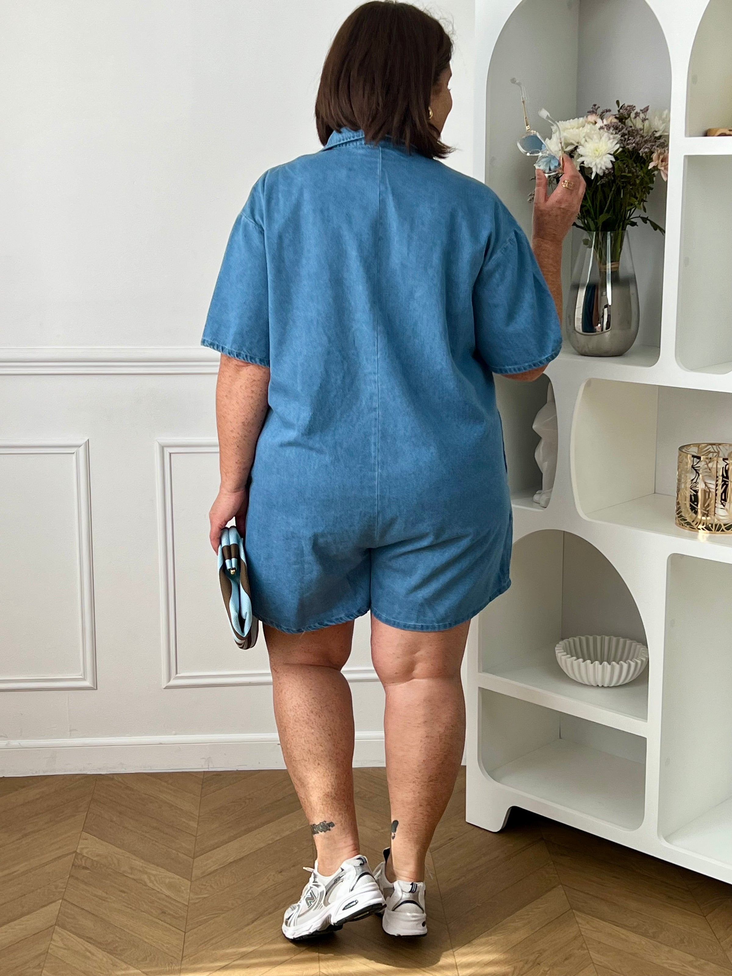 Combishort en jean grande taille, idéal pour un look casual et confortable. Doté d’un col chemise, de manches courtes et d’une coupe ample, il offre une silhouette moderne et décontractée. Avec sa poche poitrine, ses deux poches latérales et ses boutons jusqu’à mi-longueur, il allie style et praticité. Confectionné en 100% coton, ce combishort bleu est parfait pour une tenue tendance au quotidien.