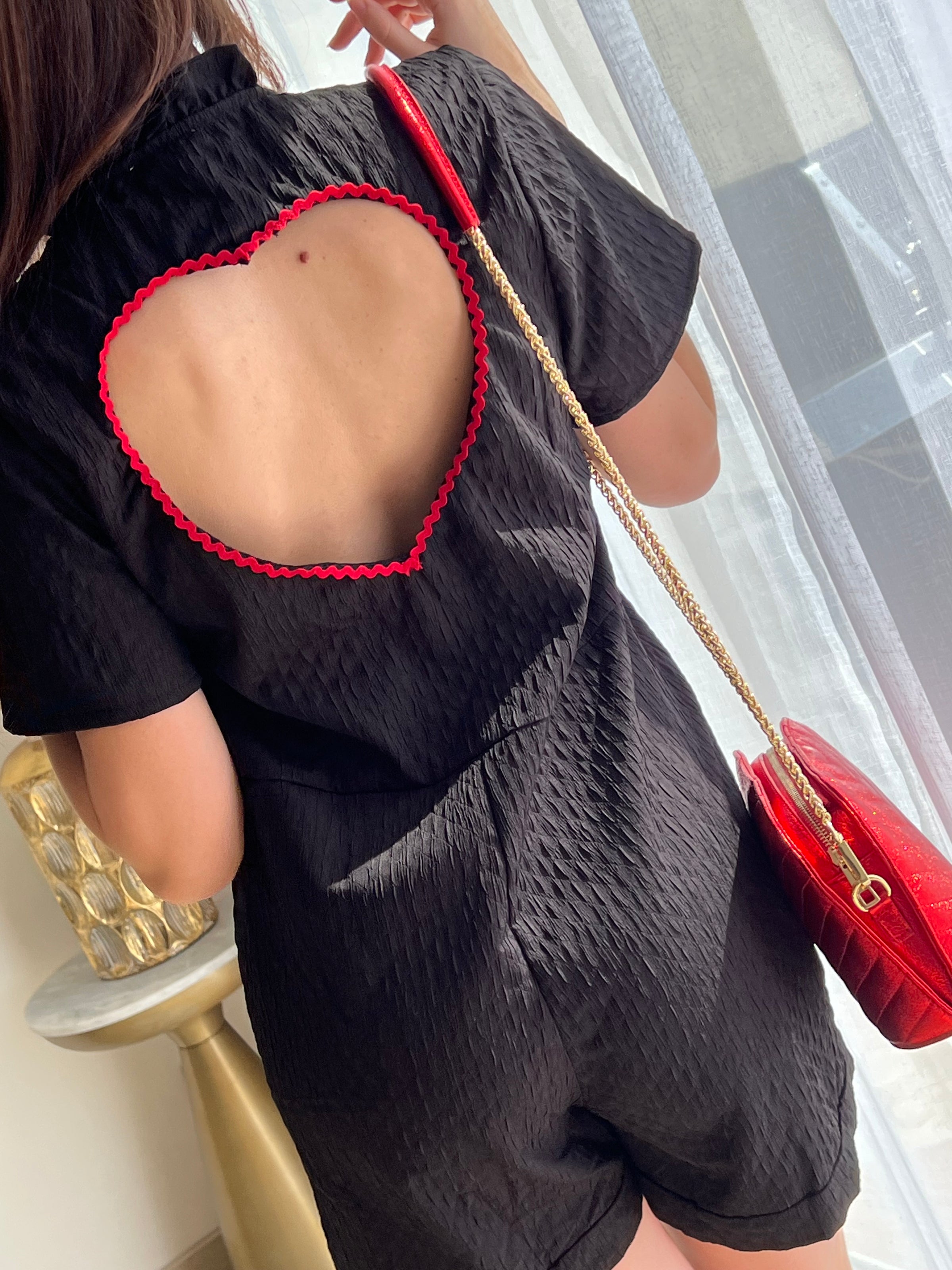 Combishort noir pour femme au design élégant et féminin, avec dos nu orné d’un cœur rouge pour une touche originale. Doté de manches courtes, d’un col montant à volants et de boutons dorés sur toute la longueur, il allie chic et modernité. Sa combinaison de couleurs noir et rouge en fait une pièce idéale pour un look sophistiqué et tendance.