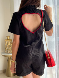 Combishort noir pour femme au design élégant et féminin, avec dos nu orné d’un cœur rouge pour une touche originale. Doté de manches courtes, d’un col montant à volants et de boutons dorés sur toute la longueur, il allie chic et modernité. Sa combinaison de couleurs noir et rouge en fait une pièce idéale pour un look sophistiqué et tendance.