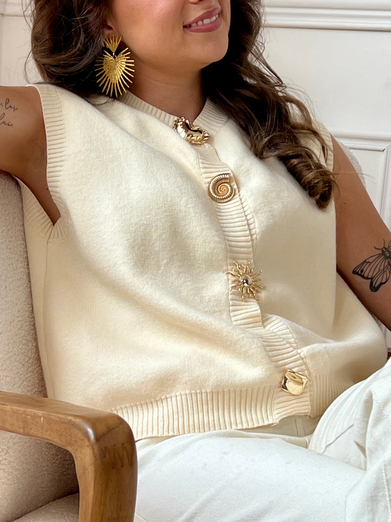 Gilet beige tout en douceur, subtilement rehaussé de détails dorés le long de la silhouette. Une pièce élégante et lumineuse, idéale pour réchauffer vos looks avec raffinement.