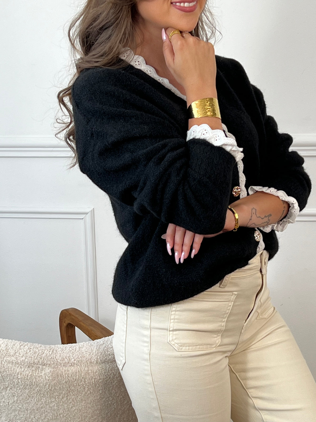 Gilet noir élégant, orné de boutons argentés aux reflets dorés subtils. Le col et les poignets se distinguent par de délicats détails festonnés en écru, apportant une touche raffinée et contrastée.
