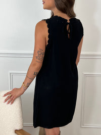 La robe courte noire Floriane est sans manches, avec un col rond devant et derrière. Ses détails festonnés et son ouverture dos avec lien à nouer ajoutent une touche délicate et féminine.