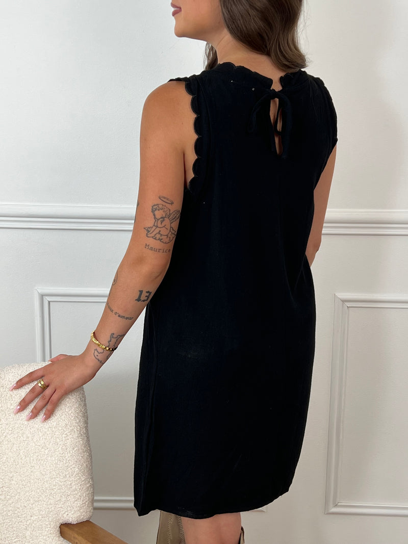 La robe courte noire Floriane est sans manches, avec un col rond devant et derrière. Ses détails festonnés et son ouverture dos avec lien à nouer ajoutent une touche délicate et féminine.