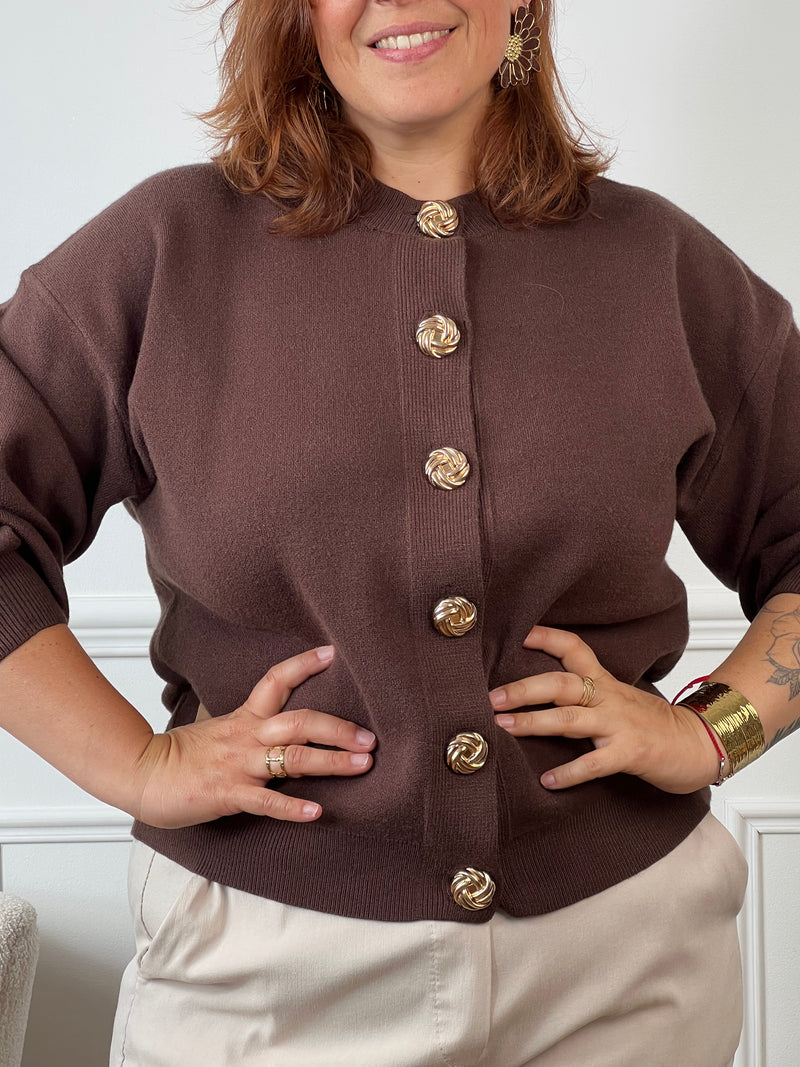 Ce gilet marron présente une coupe courte et féminine. Ses manches longues et son col rond offrent confort et élégance. Les boutons dorés sur le devant ajoutent une touche raffinée, tandis que l’étiquette discrète sur un côté souligne son authenticité.