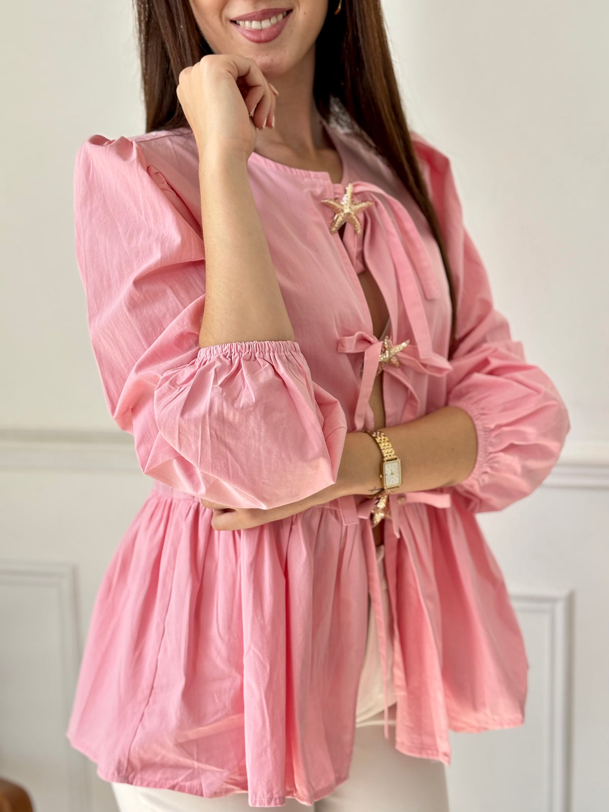 Cette blouse rose Adalia allie élégance et confort avec ses manches longues bouffantes, son col rond et ses poignets élastiques. Les liens à nouer sur le devant et les volants délicats sur le bas apportent une touche féminine et raffinée, idéale pour sublimer votre style au quotidien.