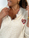 Ce pull beige grande taille allie douceur et élégance avec ses manches longues et son col en V orné de délicats motifs floraux. Un coeur brodé vient sublimer le devant, apportant une touche unique et féminine