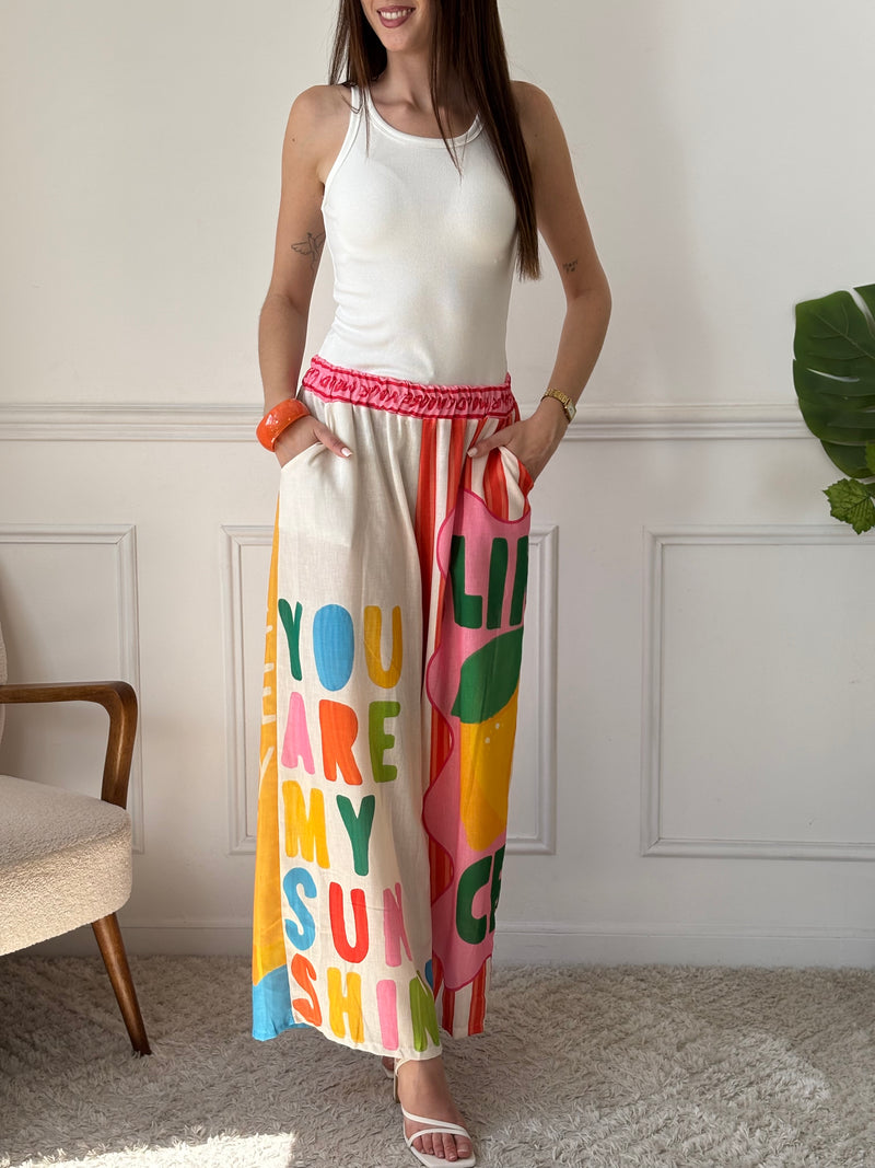 Ce pantalon en lin aux motifs colorés et inspirés des vacances respire la bonne humeur. Avec ses inscriptions comme "You are my Sunshine", "Lemoncello" ou "You are the Sunshine in everyday", il invite à la détente et à l’évasion. Ses teintes de beige, vert, orange, rose, rouge et bleu en font une pièce pétillante, idéale pour un look estival plein de charme et de légèreté.