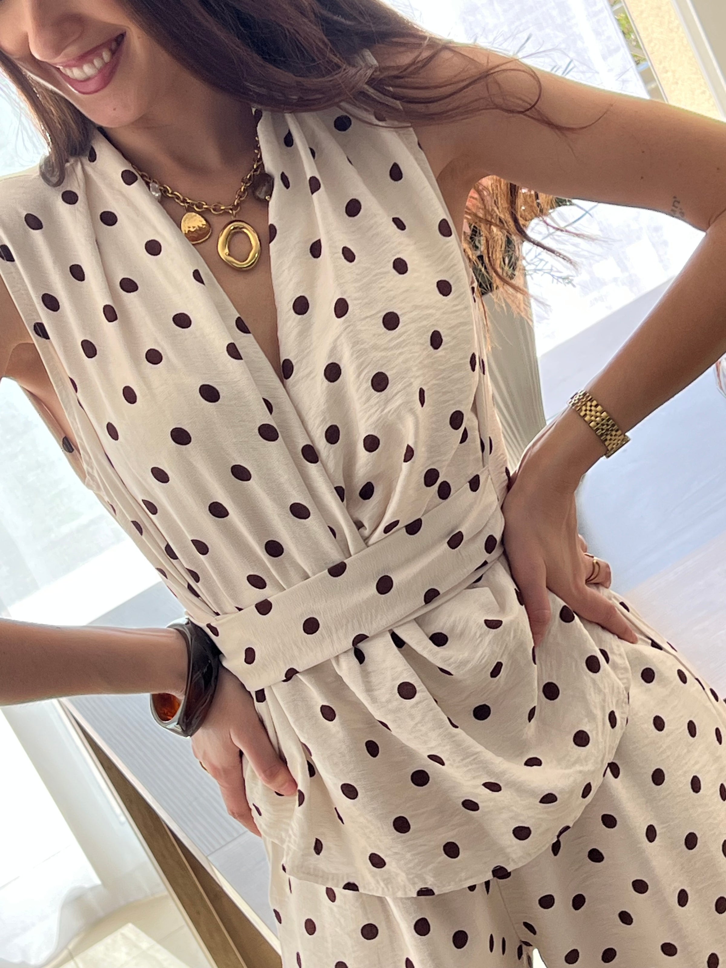 Ensemble femme élégant composé d’un top sans manches à col cache-cœur avec lien à la taille et d’un pantalon fluide assorti à pois. Sa teinte beige à pois marron apporte une touche chic et intemporelle. Fabriqué en Italie, cet ensemble est idéal pour un look raffiné au quotidien.