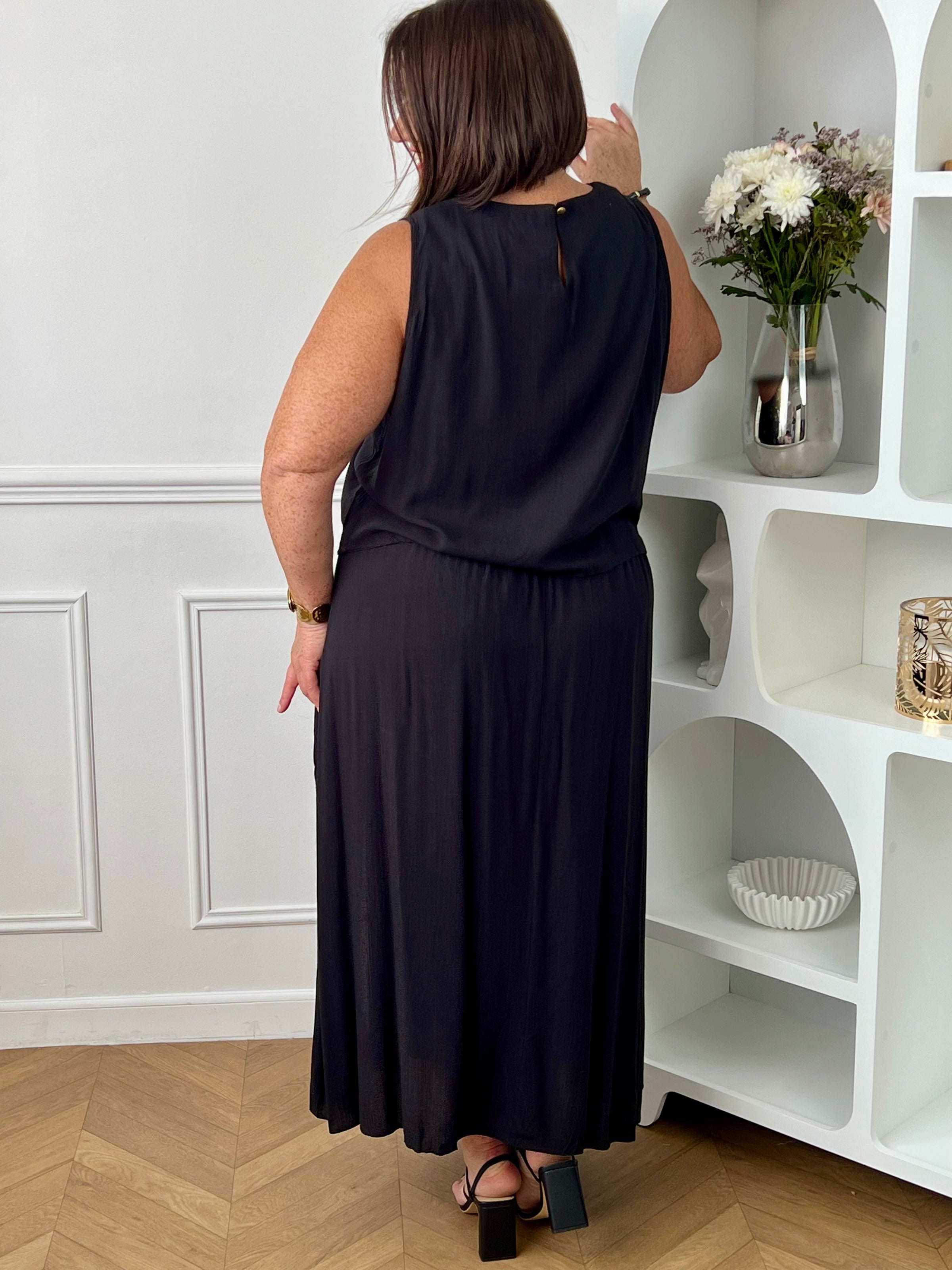 Craquez pour cet ensemble blouse et jupe noire grande taille au style élégant et raffiné. La jupe longue à coupe fluide se distingue par sa fente sur le côté, sa tresse à la taille et son élastique au dos pour un confort optimal. La blouse sans manches, dotée d’un col rond avec détail tressé et d’une ouverture au dos avec bouton, apporte une touche féminine et sophistiquée.