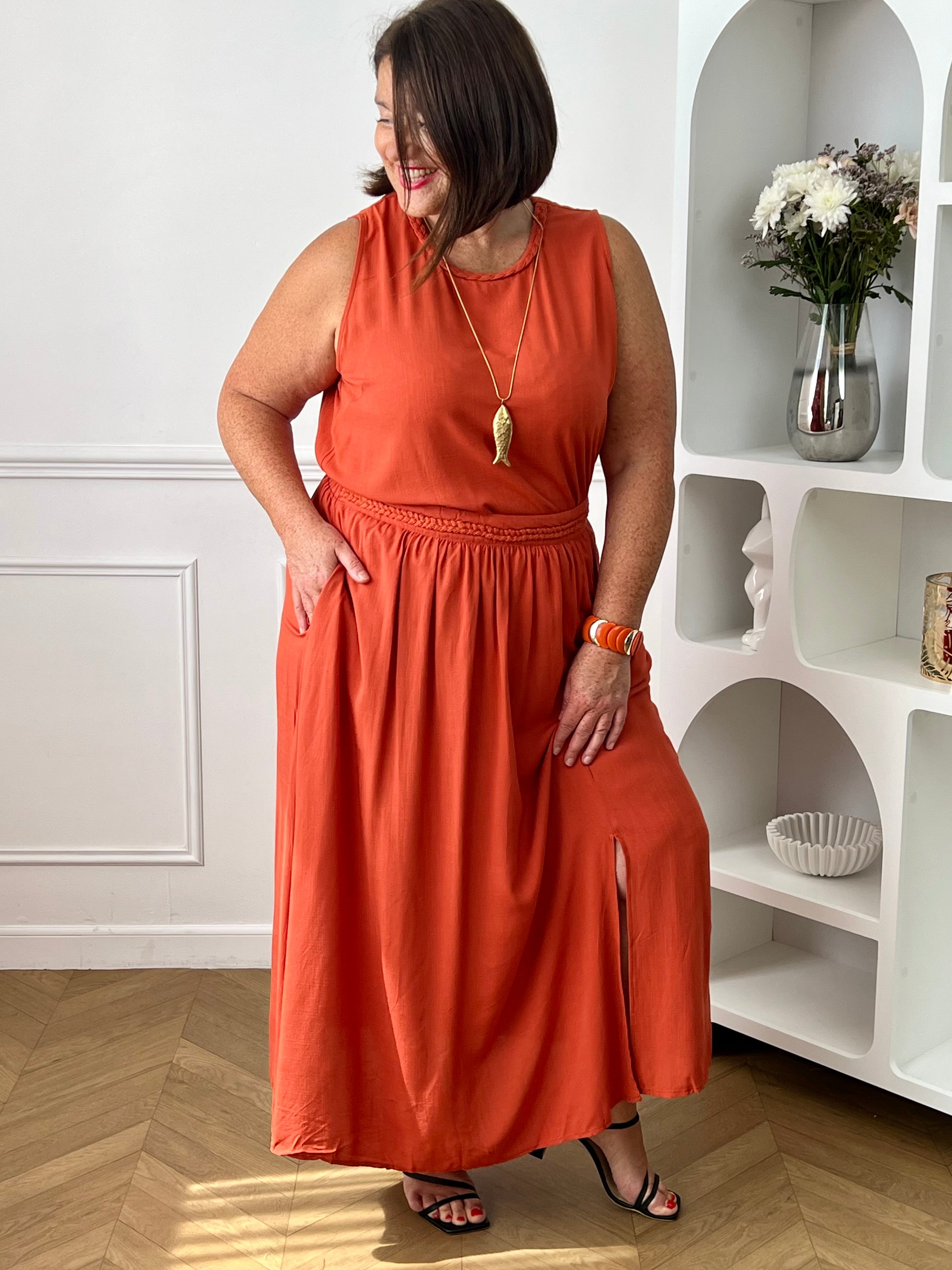 Craquez pour cet ensemble blouse et jupe terracotta grande taille au style élégant et raffiné. La jupe longue à coupe fluide se distingue par sa fente sur le côté, sa tresse à la taille et son élastique au dos pour un confort optimal. La blouse sans manches, dotée d’un col rond avec détail tressé et d’une ouverture au dos avec bouton, apporte une touche féminine et sophistiquée.