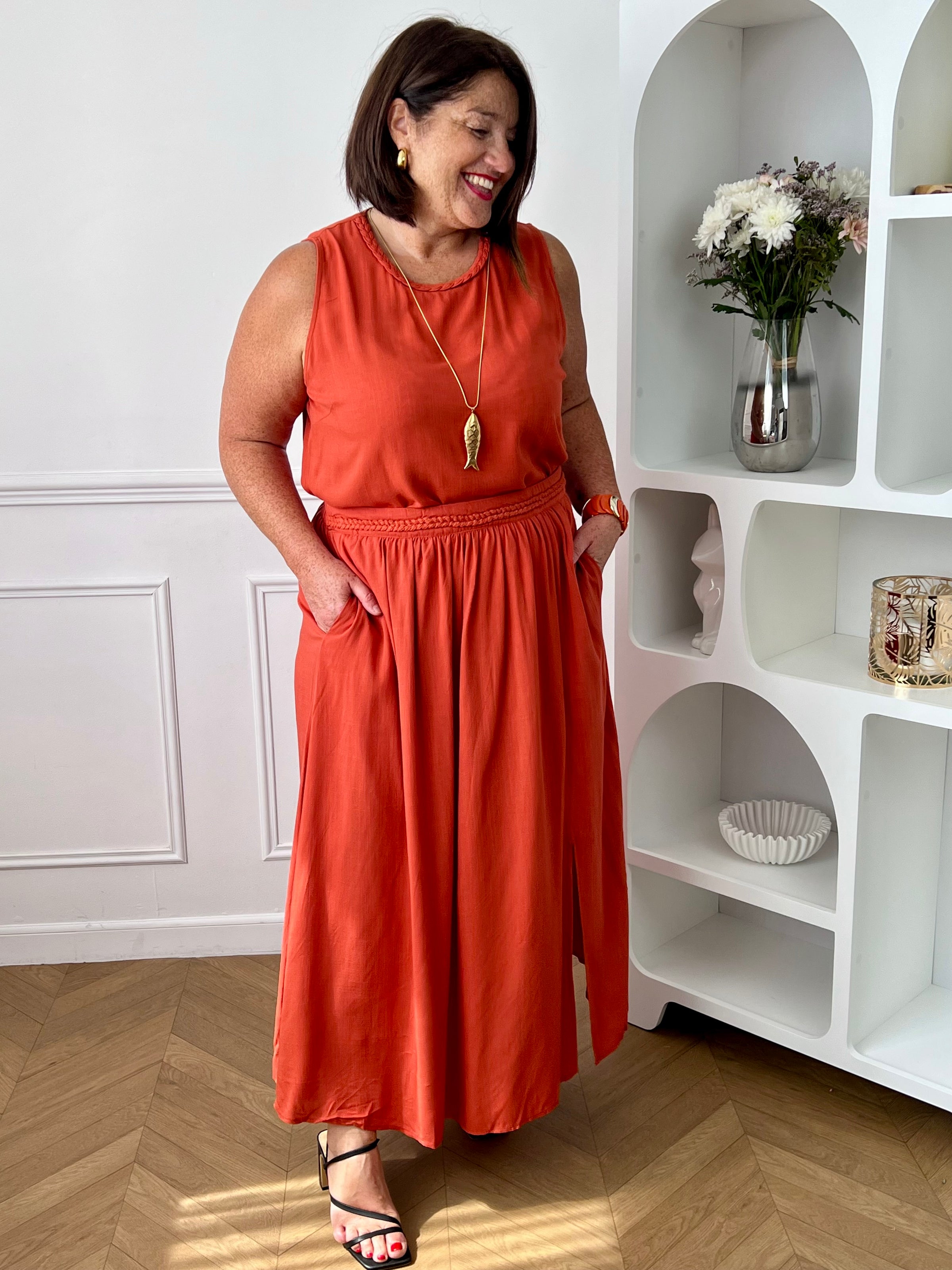 Craquez pour cet ensemble blouse et jupe terracotta grande taille au style élégant et raffiné. La jupe longue à coupe fluide se distingue par sa fente sur le côté, sa tresse à la taille et son élastique au dos pour un confort optimal. La blouse sans manches, dotée d’un col rond avec détail tressé et d’une ouverture au dos avec bouton, apporte une touche féminine et sophistiquée.
