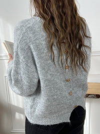 Ce pull gris Elisa est un incontournable pour votre garde-robe. Avec ses boutons dorés en forme de fleur au dos, il apporte une touche d'élégance et de fantaisie à votre tenue. 
