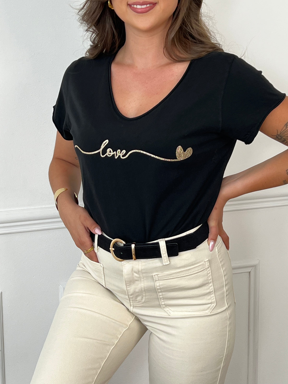 Ce tee-shirt noir "Clelia" allie confort et élégance avec ses manches courtes et son col rond classique. Sa touche distinctive, une inscription dorée sur le devant, apporte une subtile note de sophistication. Idéal pour un style décontracté mais soigné au quotidien.