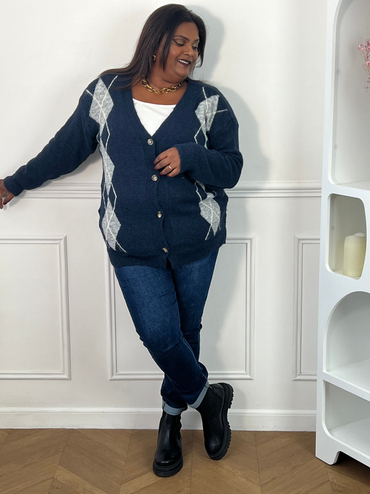 Gilet bleu à losanges gris et blancs porté boutonné avec un jean, en pose jambes croisées – Isadora | Loïcia