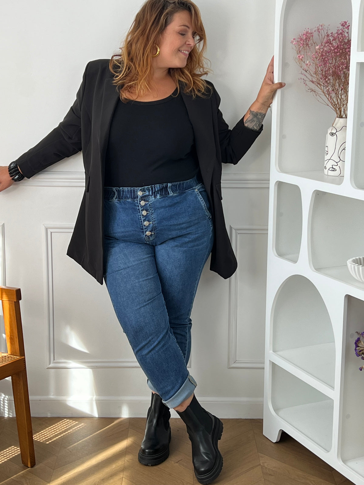 Jean bleu Felicie grande taille à boutons apparents, porté avec les bas retroussés, un blazer noir et des bottines noires.