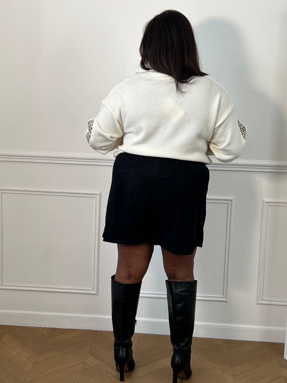 Jupe-short noire Adele portée de dos, montrant la coupe du short, avec un gilet écru et des bottes noires.