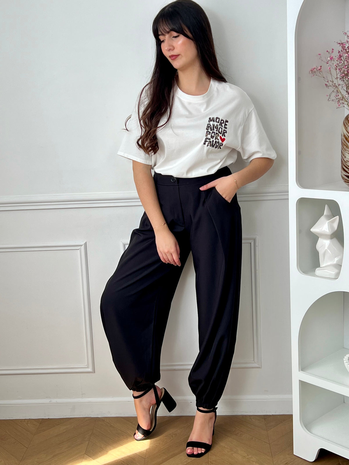 Pantalon noir femme à coupe ballon, idéal pour un look moderne et confortable. Doté de plis sur le devant, d’une taille élastique et de chevilles resserrées, il offre une silhouette tendance. Ses deux poches latérales, sa fermeture par zip et bouton ainsi que ses passants pour ceinture allient praticité et style. Facile à associer, ce pantalon noir est un incontournable du dressing féminin.
