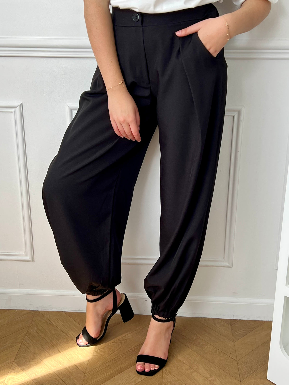 Pantalon noir femme à coupe ballon, idéal pour un look moderne et confortable. Doté de plis sur le devant, d’une taille élastique et de chevilles resserrées, il offre une silhouette tendance. Ses deux poches latérales, sa fermeture par zip et bouton ainsi que ses passants pour ceinture allient praticité et style. Facile à associer, ce pantalon noir est un incontournable du dressing féminin.