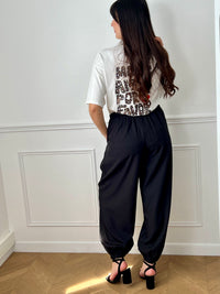 Pantalon noir femme à coupe ballon, idéal pour un look moderne et confortable. Doté de plis sur le devant, d’une taille élastique et de chevilles resserrées, il offre une silhouette tendance. Ses deux poches latérales, sa fermeture par zip et bouton ainsi que ses passants pour ceinture allient praticité et style. Facile à associer, ce pantalon noir est un incontournable du dressing féminin.