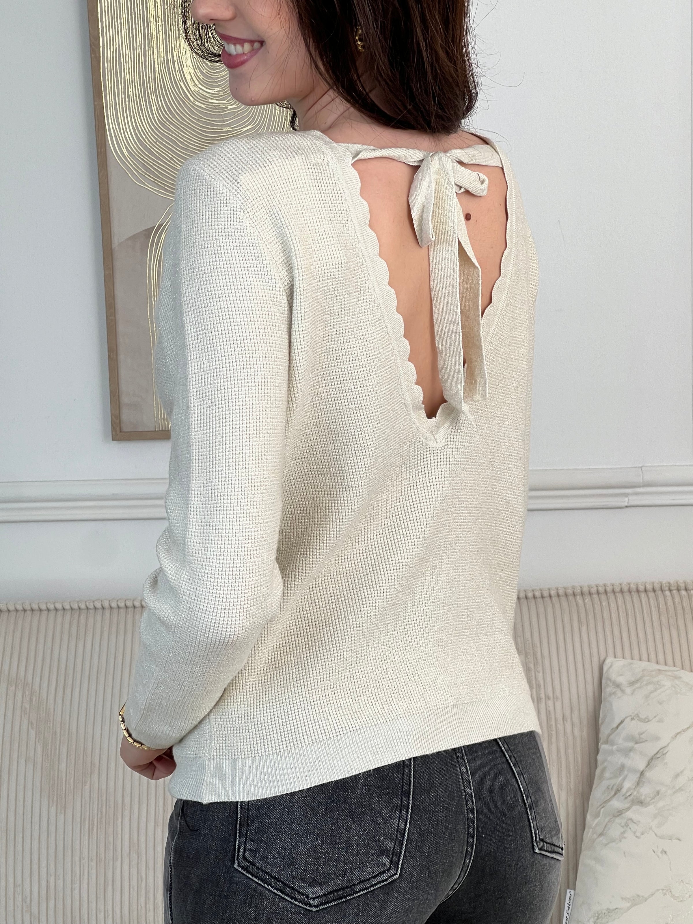 Le pull Celestina combine élégance et sensualité avec son dos nu en V à lien noué et ses manches longues. Orné de fil lurex doré, ce pull beige et doré brille de mille feux. Son col rond festonné ajoute une touche de raffinement pour des occasions spéciales.