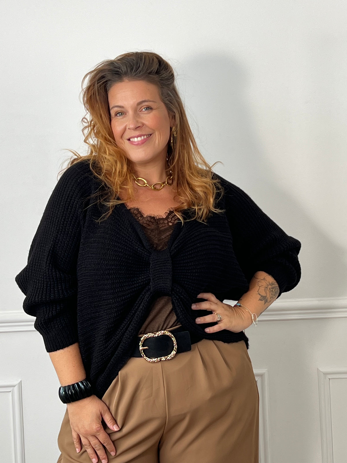 Vue rapprochée du pull noir Aelina en maille, avec détail noué sur le devant, porté sur un haut marron à dentelle.